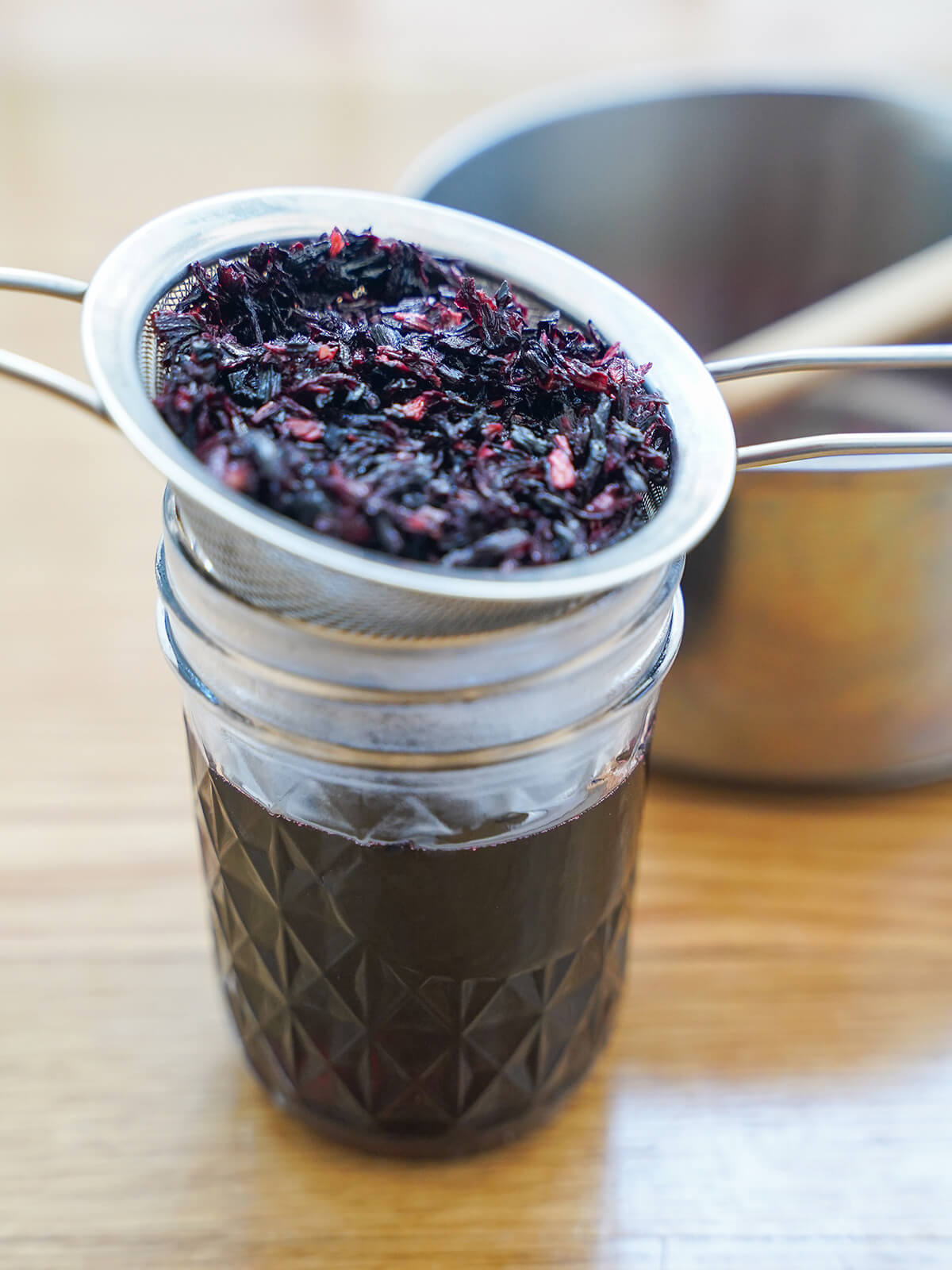 strainer over jar holding hibiscus flowers with syrup drained through into jar.