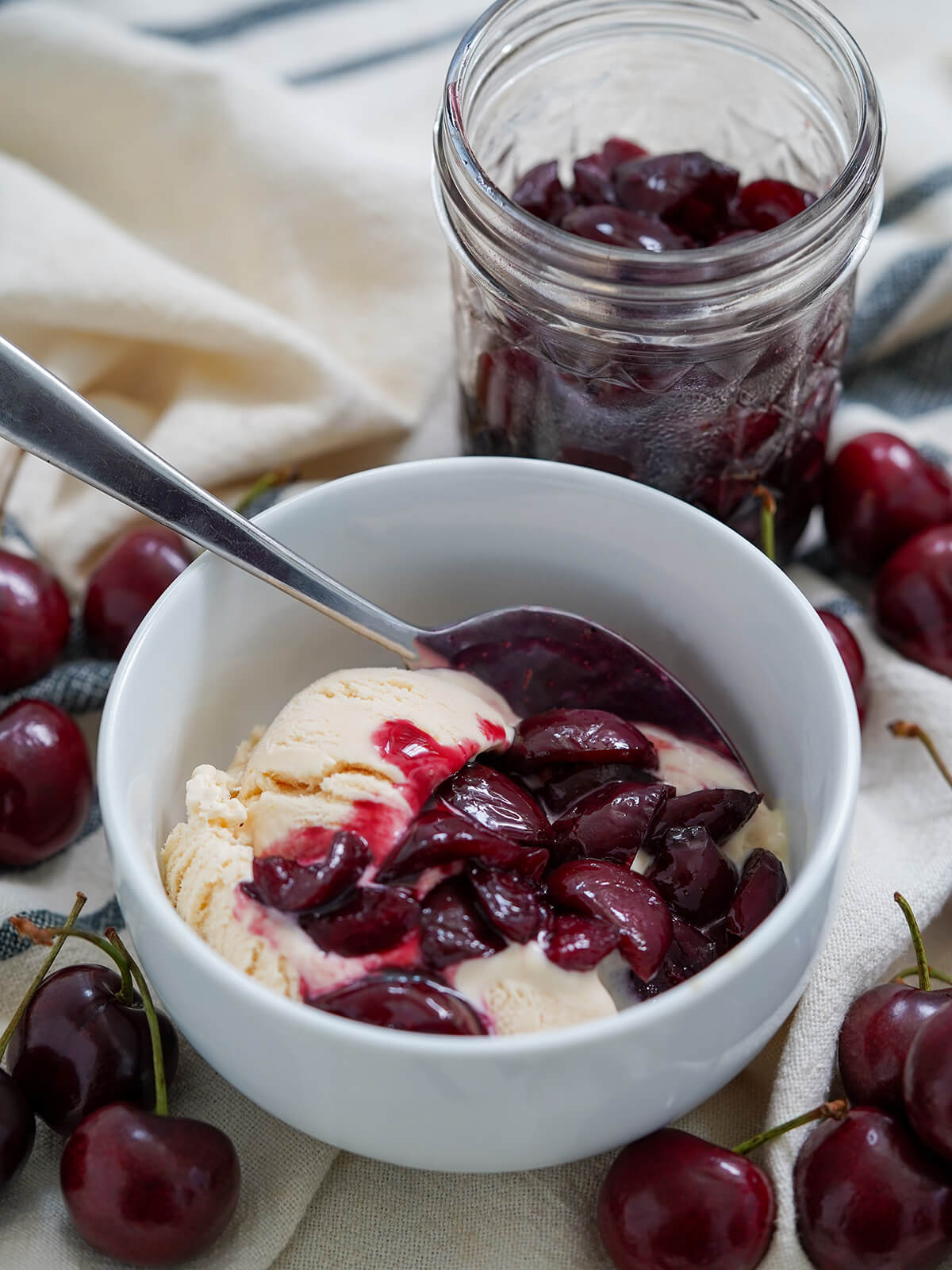 cherry compote served ver ice cream with jar behind and cherries around.