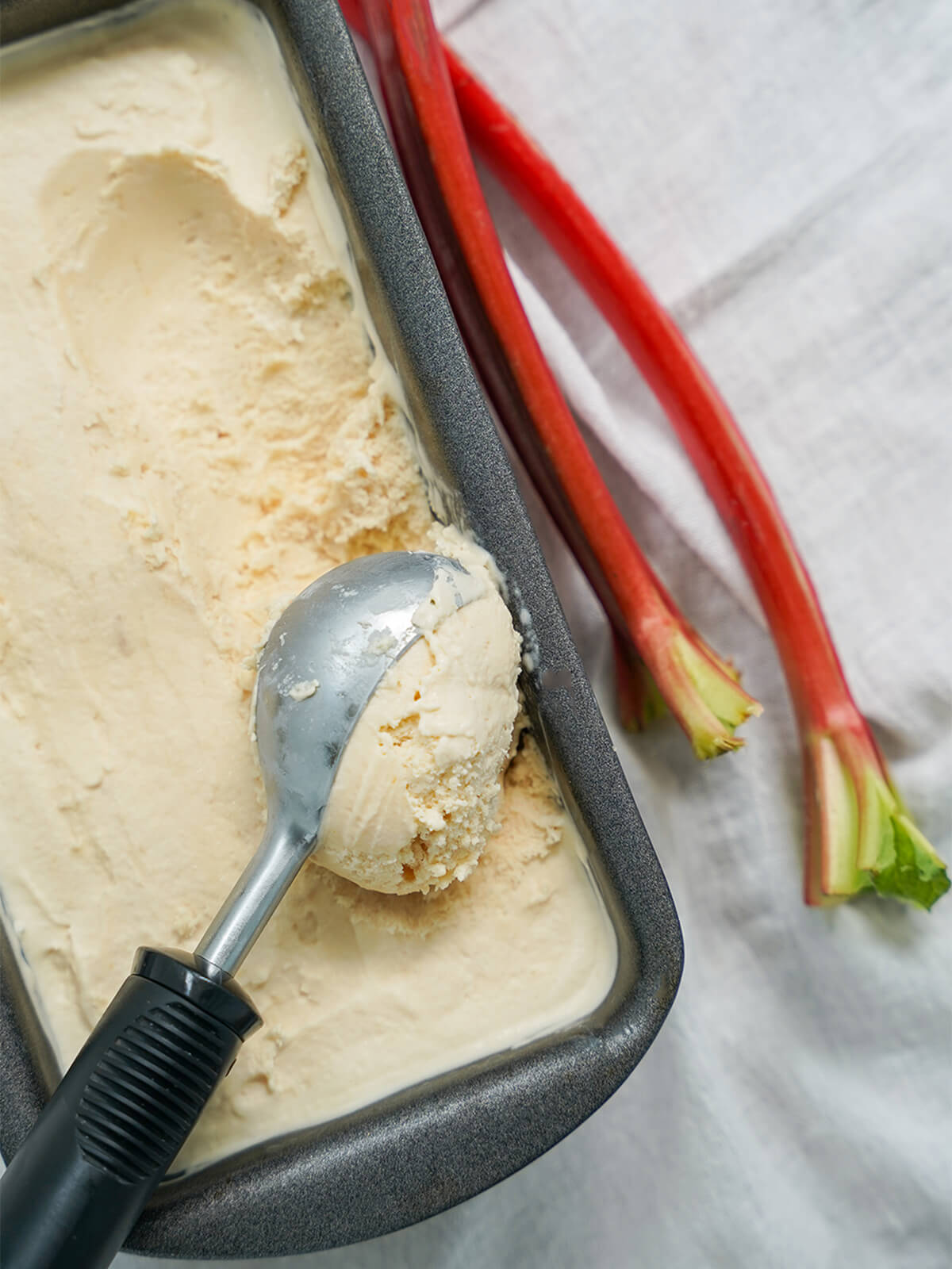 ice cream scoop taking scoop from tin of rhubarb ice cream.