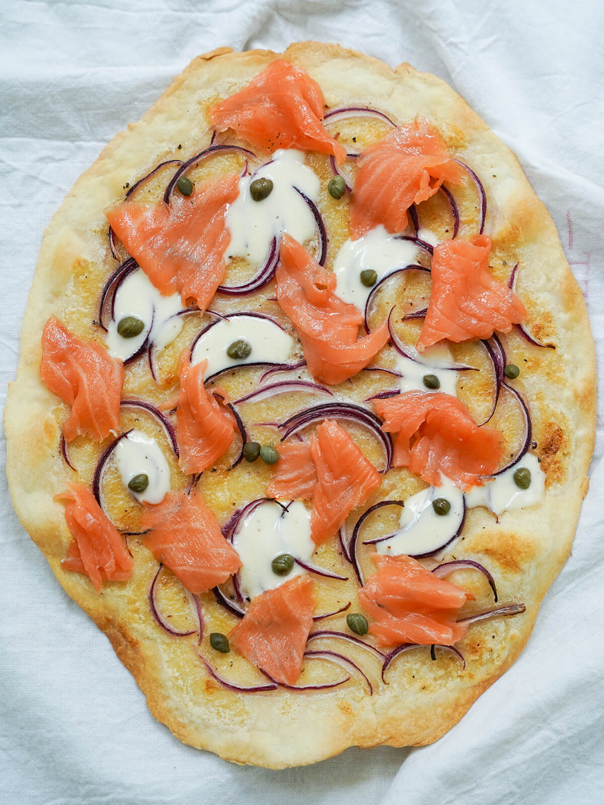 This smoked salmon pizza is a simple, tasty combination of a crisp base topped with delicate smoked salmon, creamy creme fraiche and a scatter of onion and capers. It's easy, flavorful and versatile when you serve it. smoked salmon pizza from overhead.