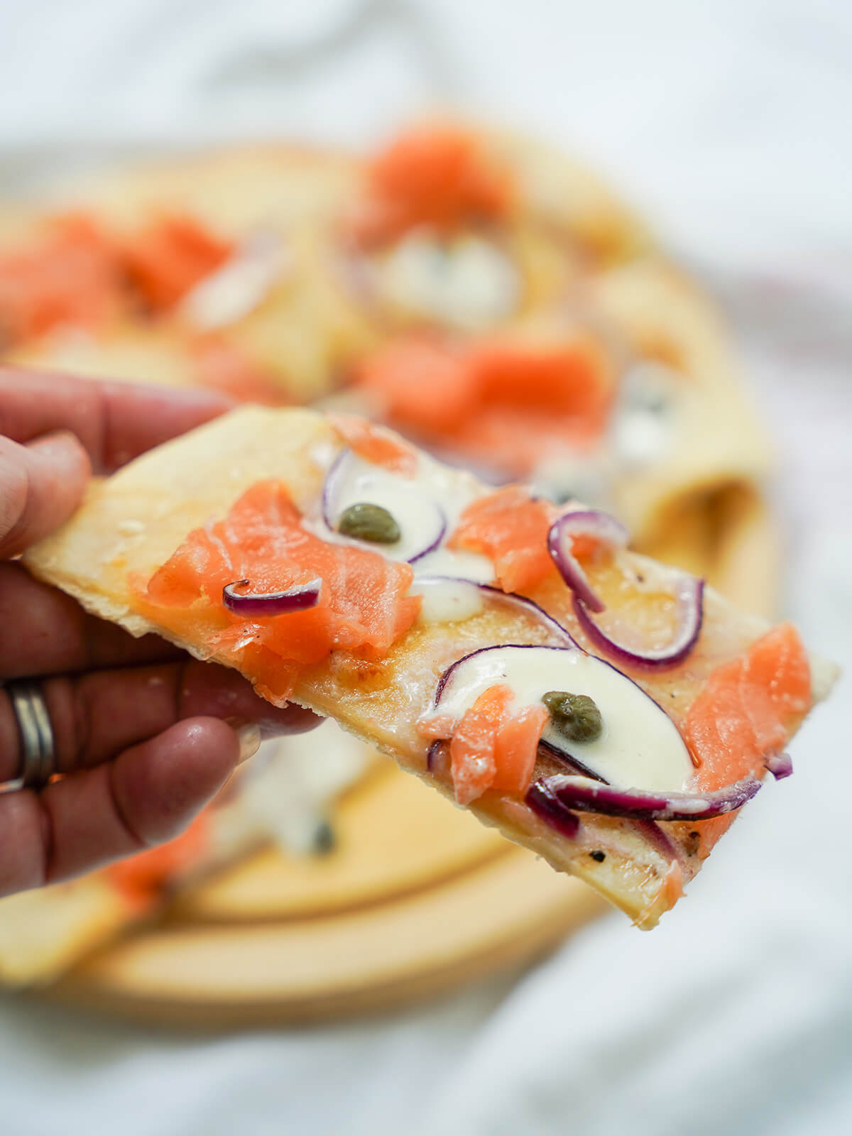 slice of smoked salmon pizza holding a slice of smoked salmon pizza in hand over board with rest.