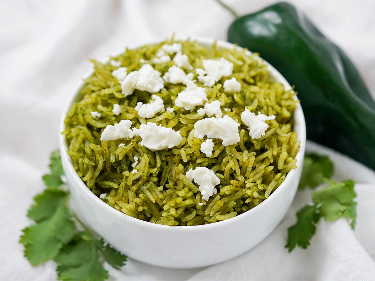 bowl of arroz verde, Mexican green rice, with poblano pepper in background and cilantro either side of bowl.