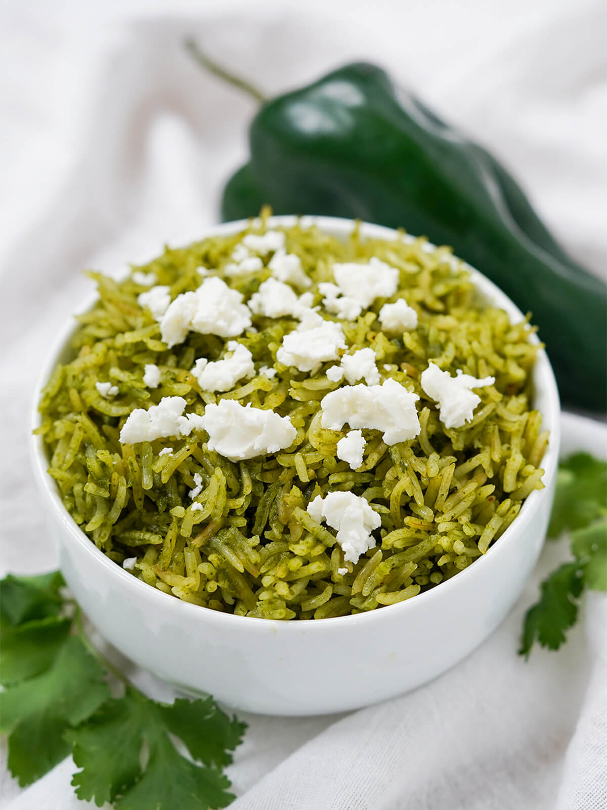 bowl of arroz verde Mexican green rice with poblano behind and cilantro in front of bowl.