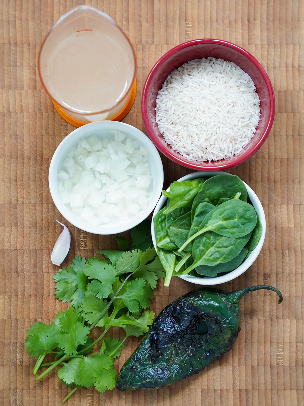 bowls of rice, onion, spinach with measure of stock, bunch of cilantro and charred poblano to side.