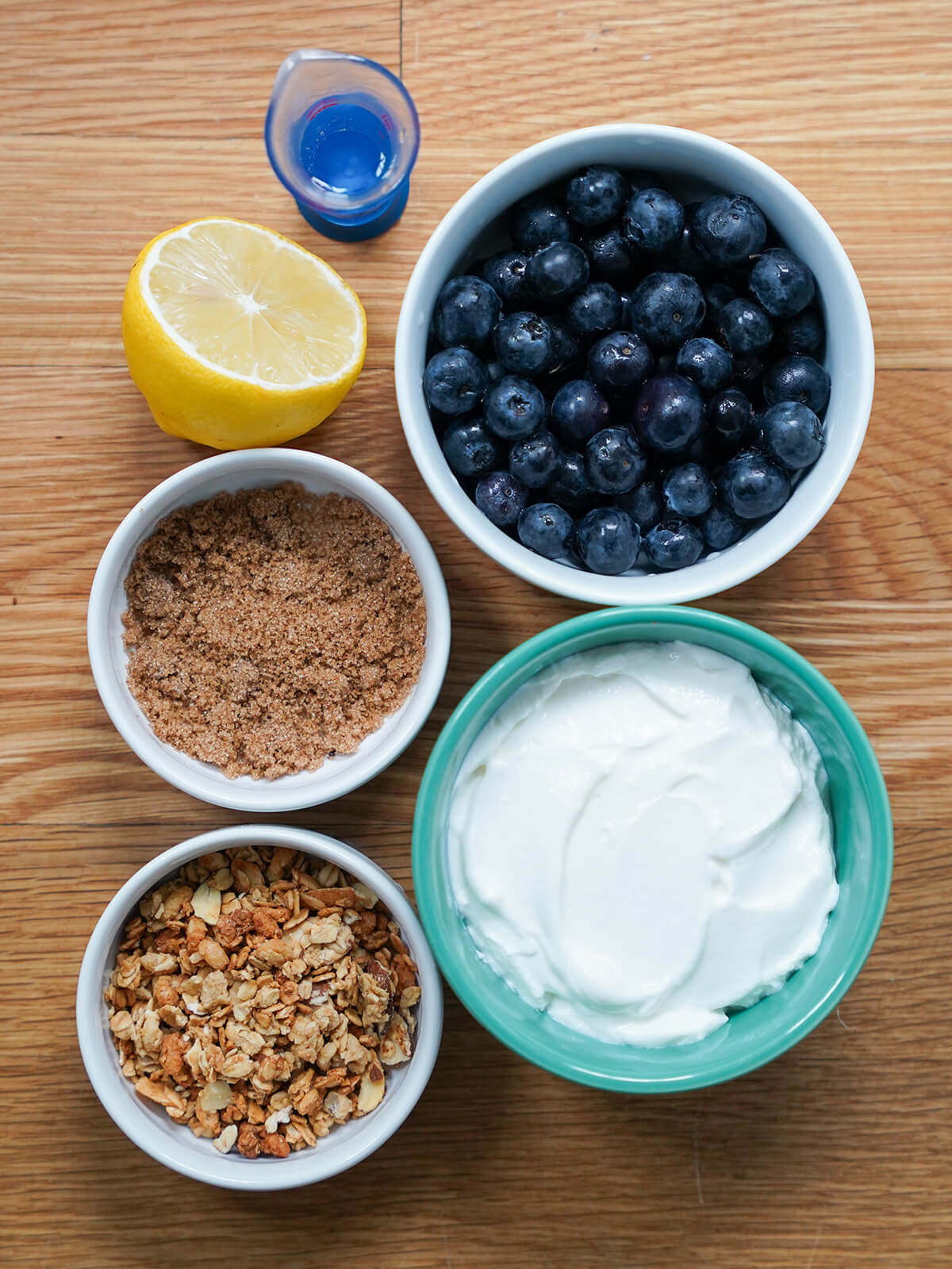 bowls of blueberries, yogurt, brown sugar, granola and part lemon from overhead.