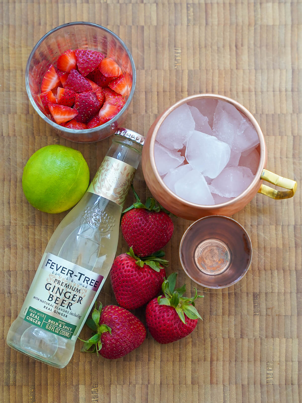 bottle of ginger beer, copper mug filled with ice, strawberries, lime, measure.