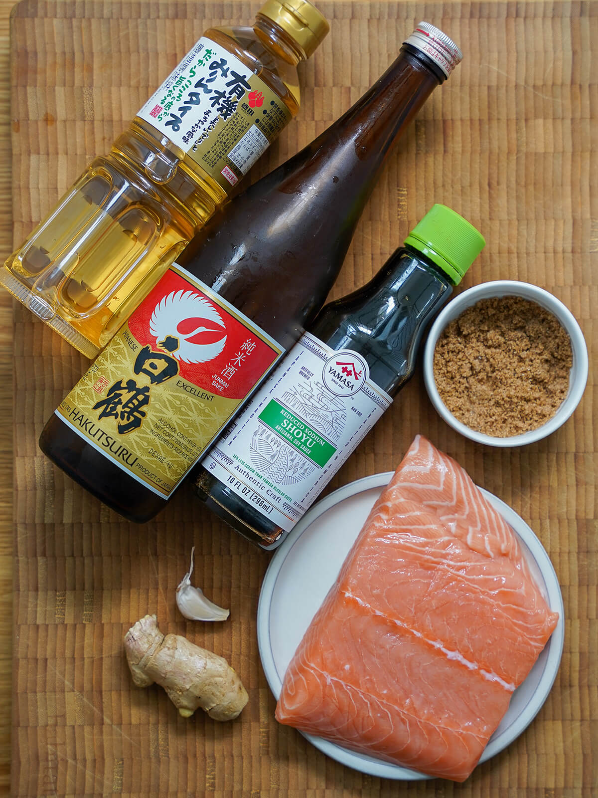 piece of salmon, small bowl of brown sugar, piece of ginger, garlic and bottles of soy, mirin and sake.