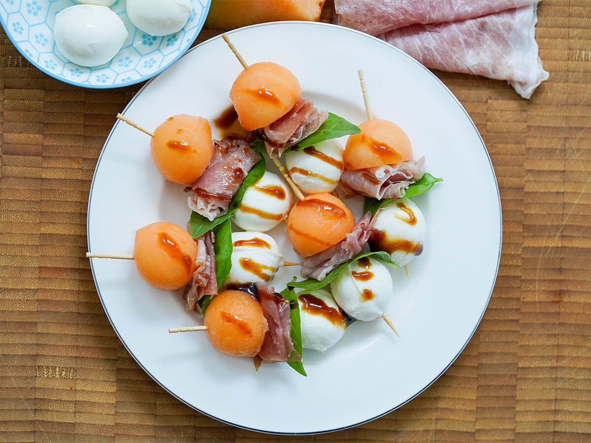 plate of melon and prosciutto skewers on wooden board.