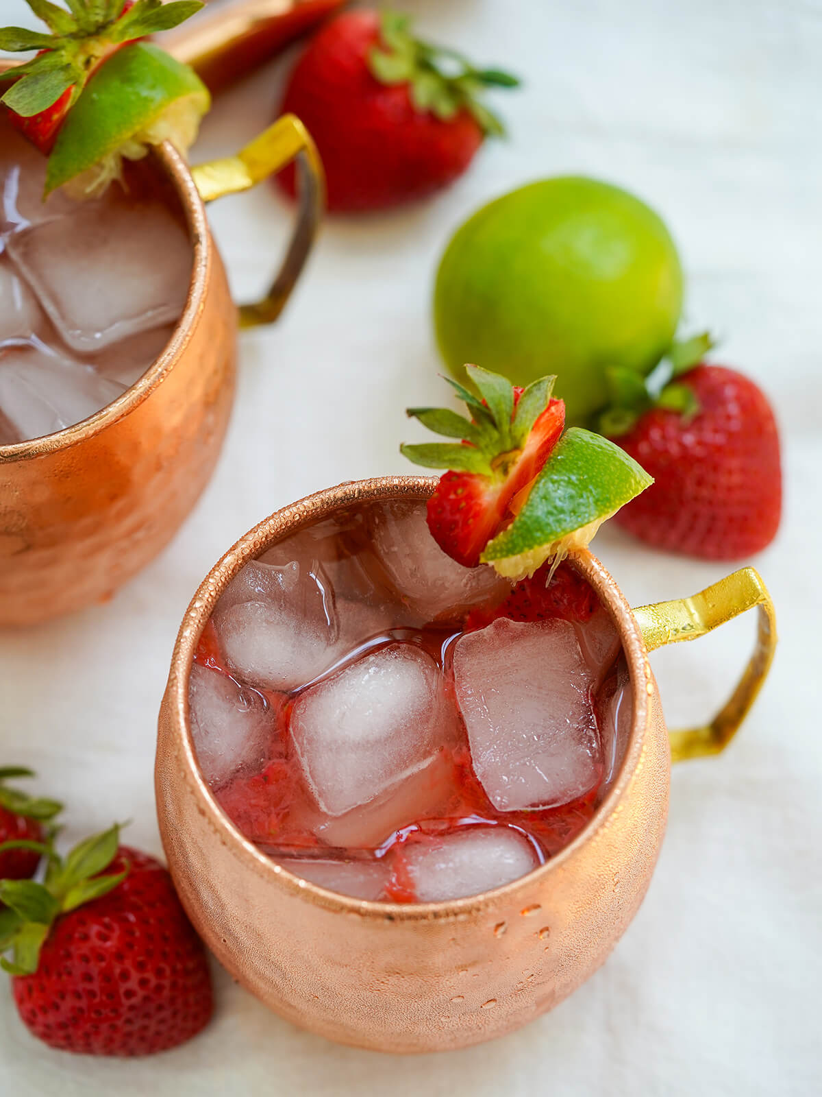 overhead view of mug of strawberry Moscow mule showing cubes of ice and strawberry and lime garnish.