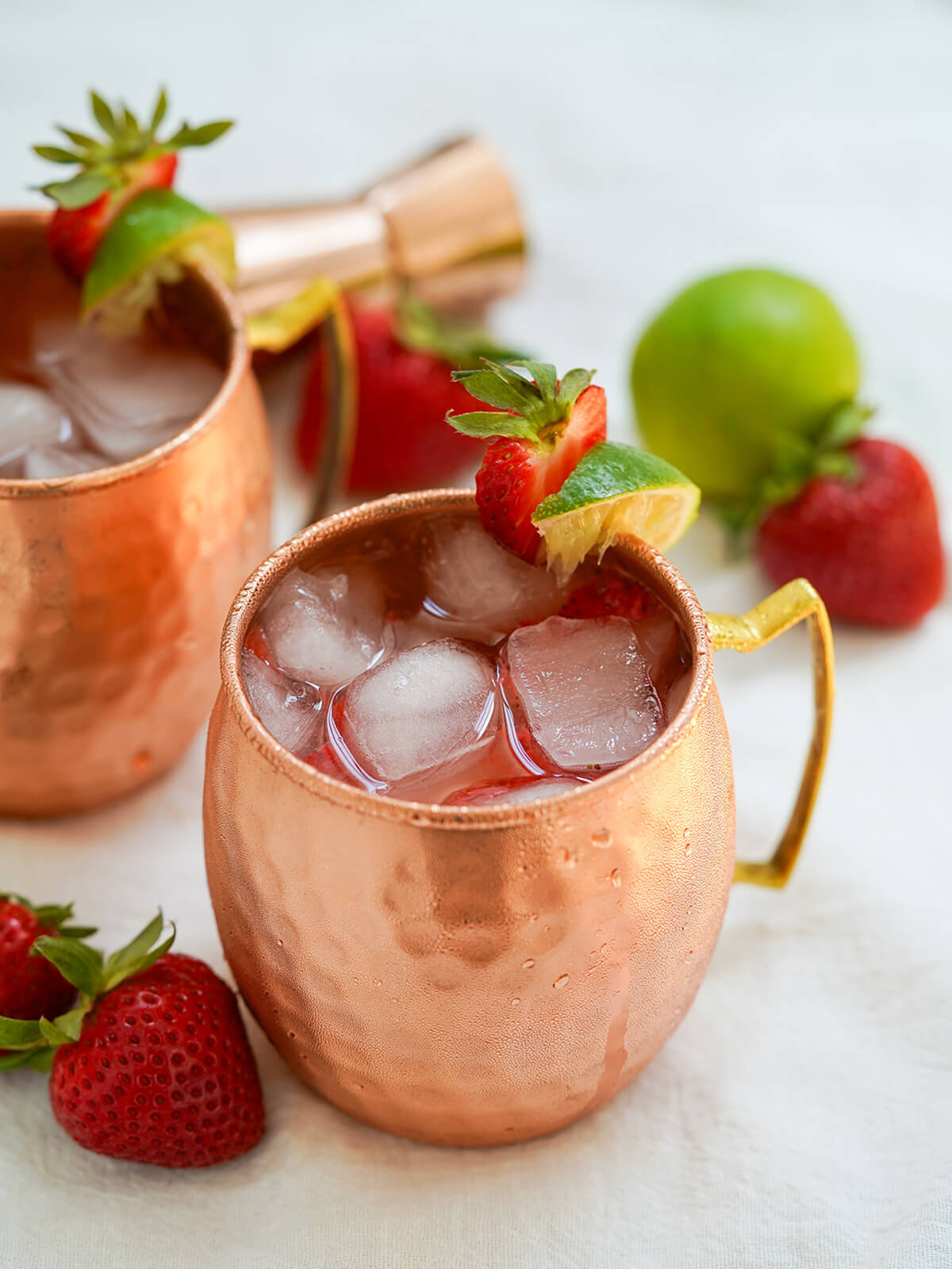 side view of copper mug of strawberry Moscow mule with strawberry to side and more behind.