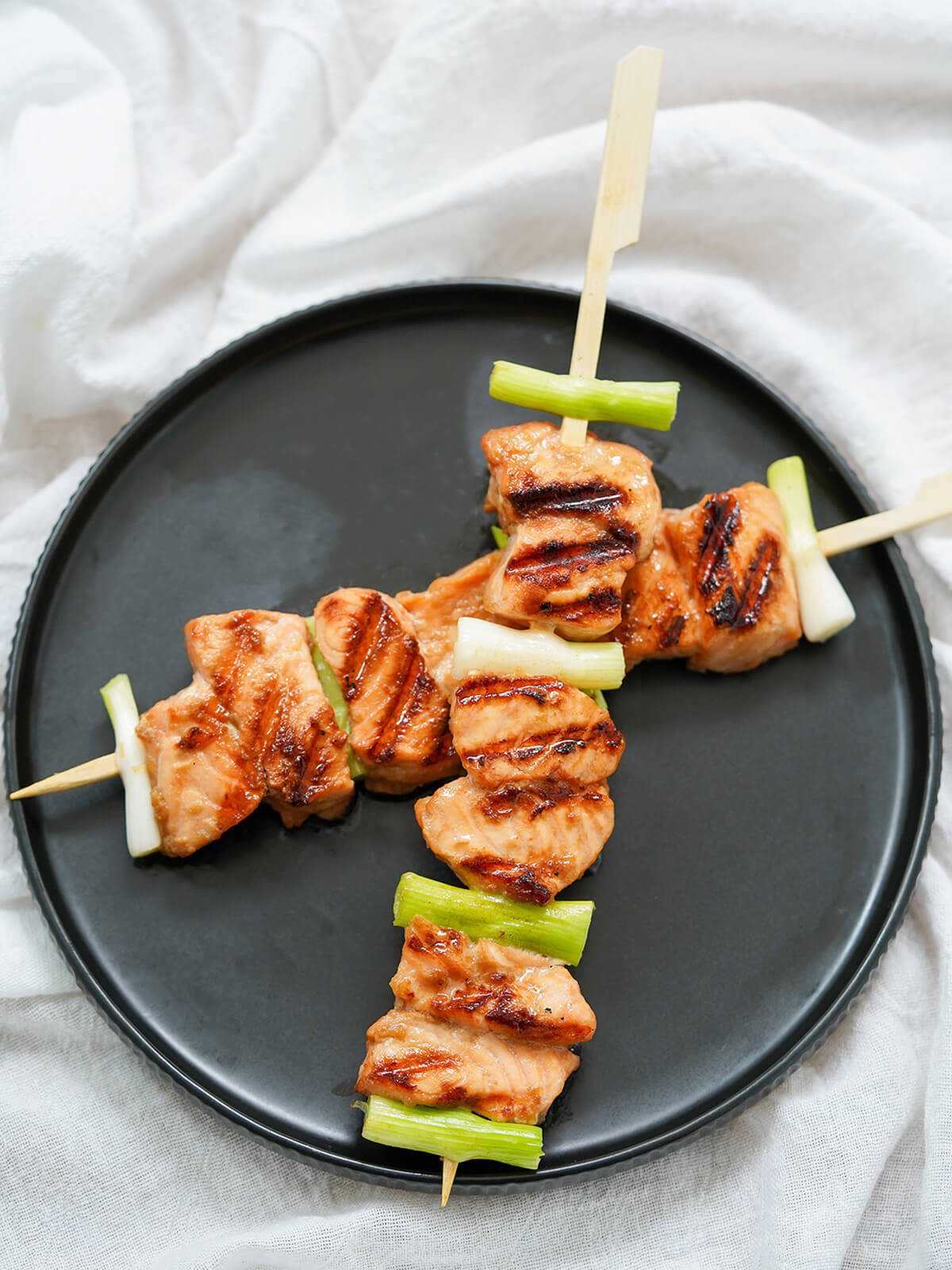 plate of two teriyaki salmon skewers overlapping each other on a black plate.