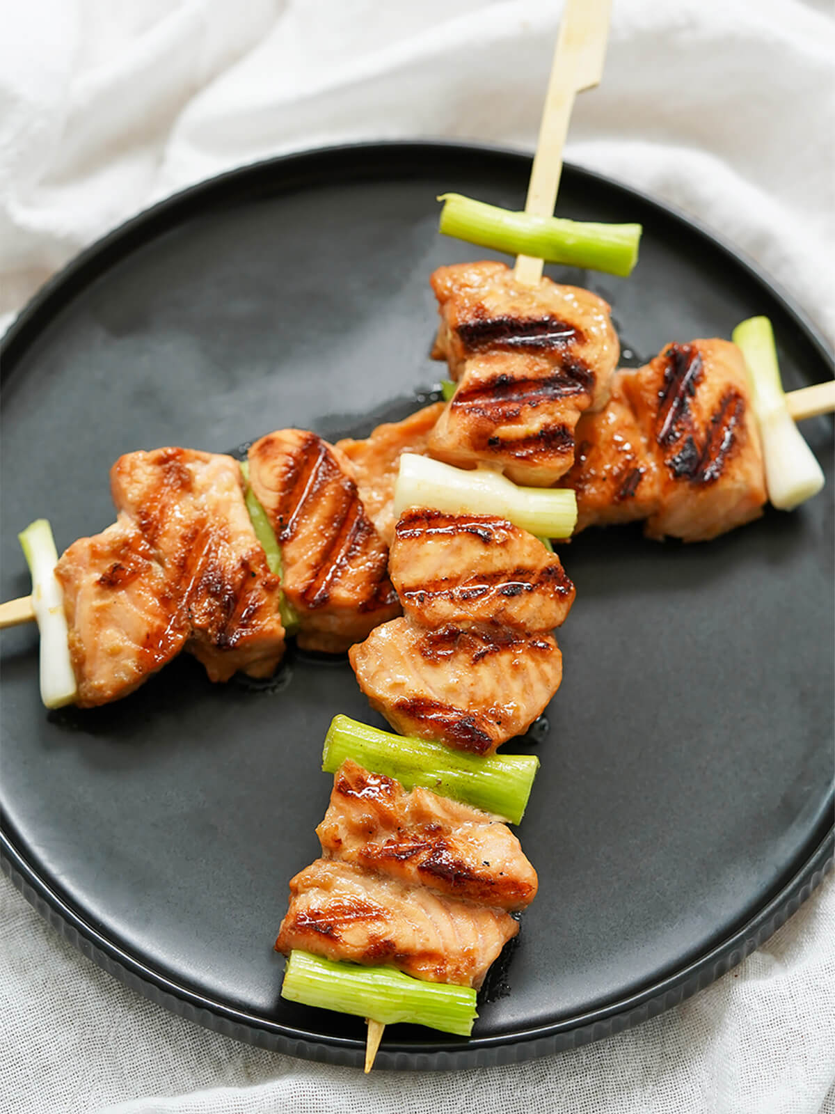 close up of two teriyaki salmon skewers with green onion between salmon pieces.