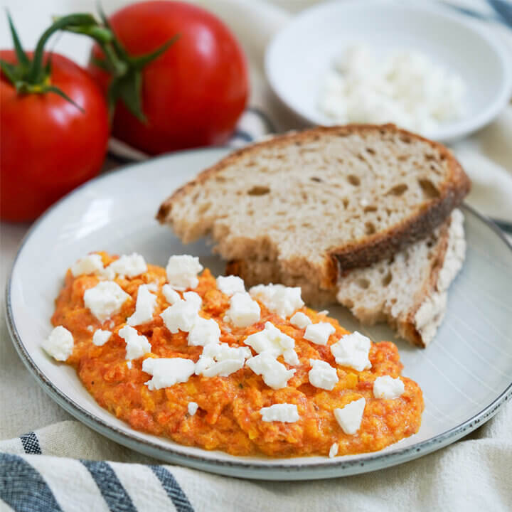 Greek eggs with tomato, strapatsada, on plate with bread at back of plate.