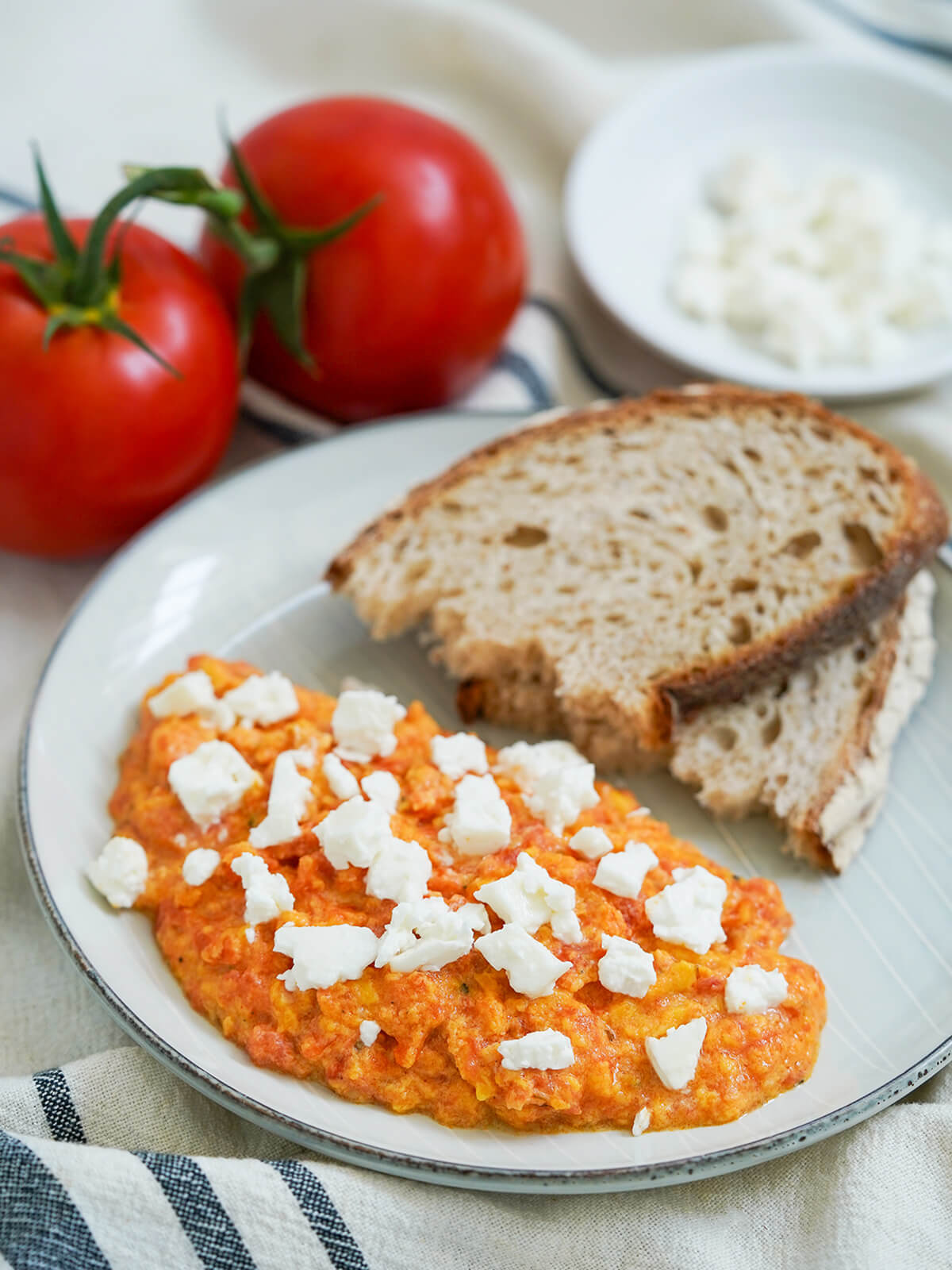 side view of Greek eggs with tomato, strapatsada, with bread to back of plate and tomatoes behind.