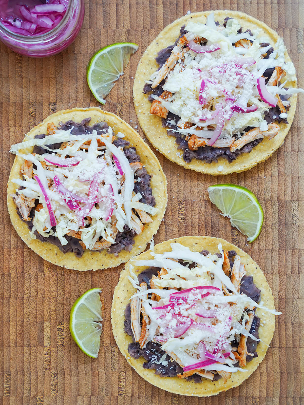 overhead view of three chicken tostadas on a wooden board.