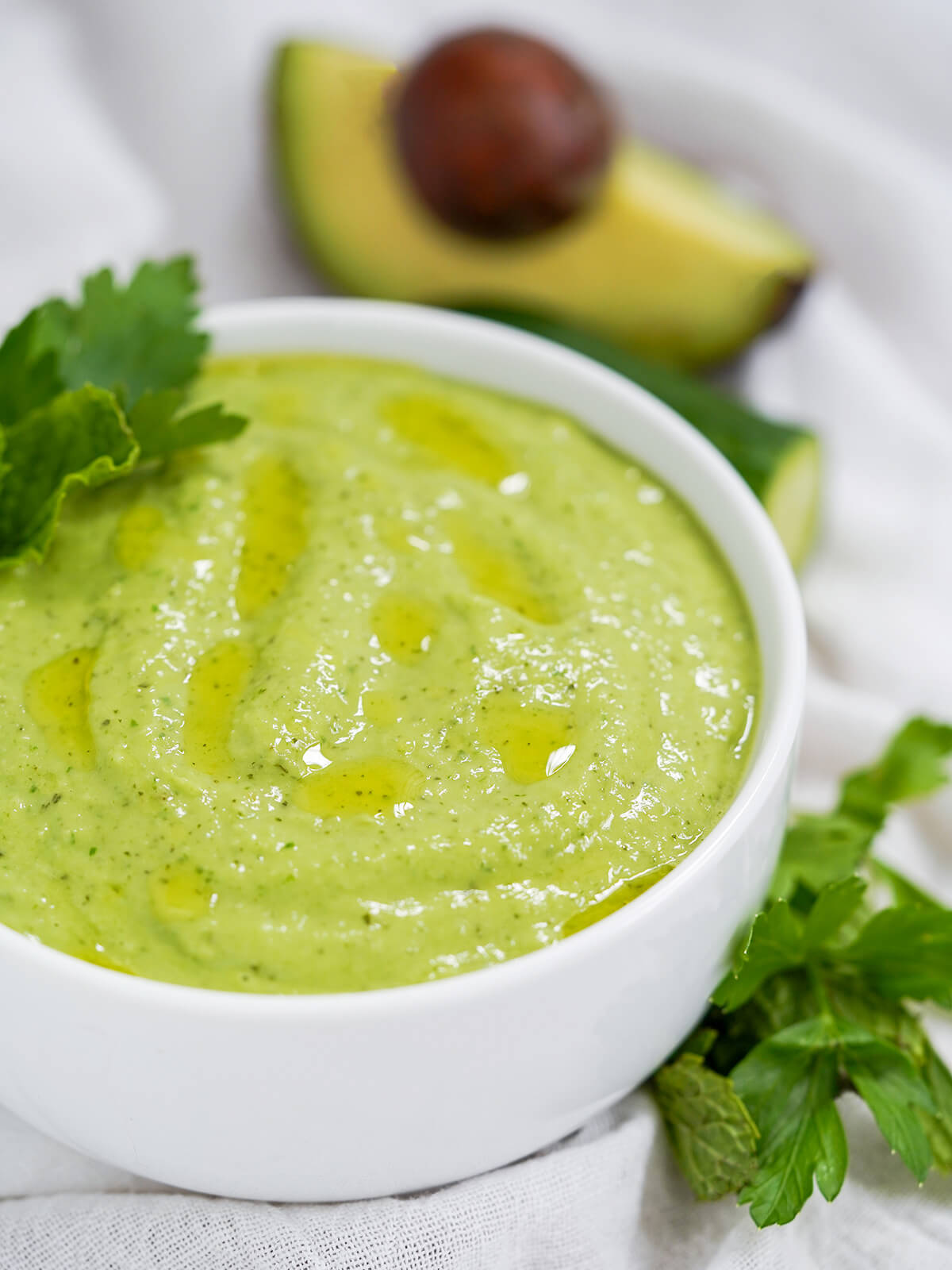 side view of bowl of cucumber avocado gazpacho (green gazpacho) with avocado in background.