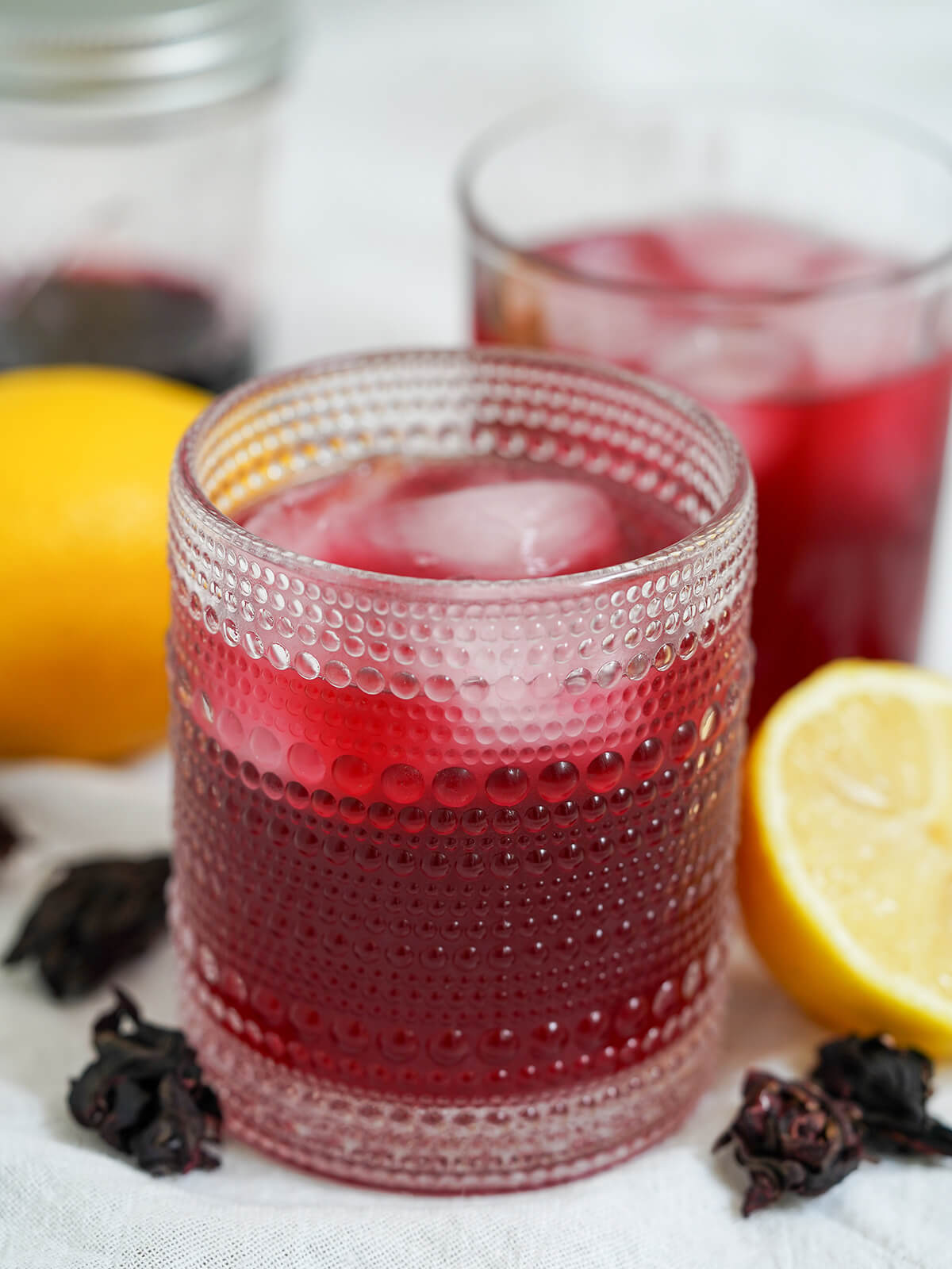 glass of hibiscus lemonade with another blurred in background and part of lemons in view.