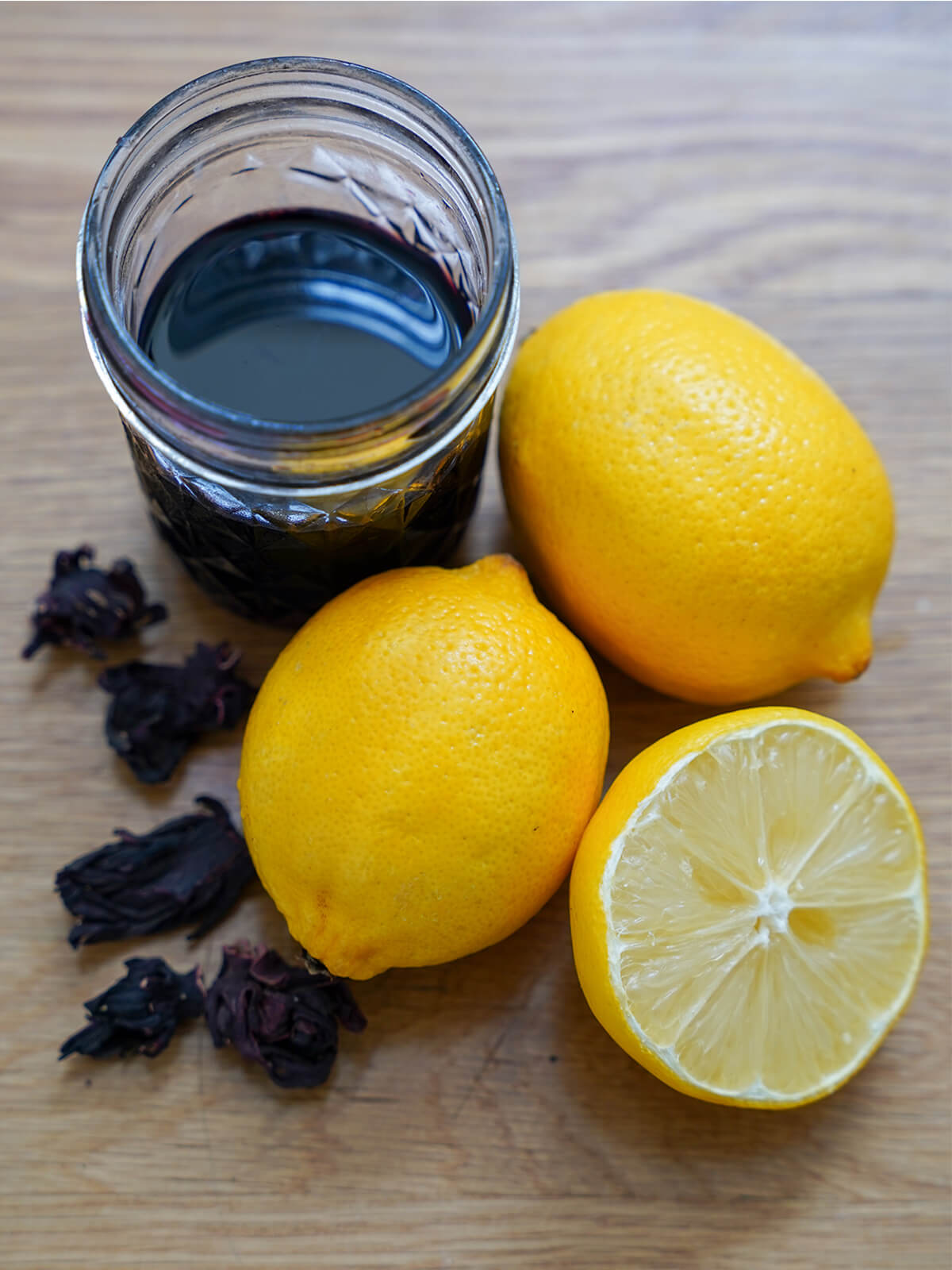 two whole lemons, cut lemon and jar of hibiscus syrup and hibiscus flowers to side.
