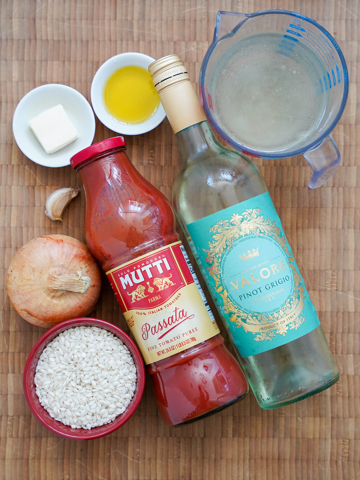 bottles of passata and white wine, measure with stock, dishes with arborio rice, oil and butter and onion and garlic to side.