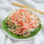 plate of kani salad from side with chopsticks behind plate.
