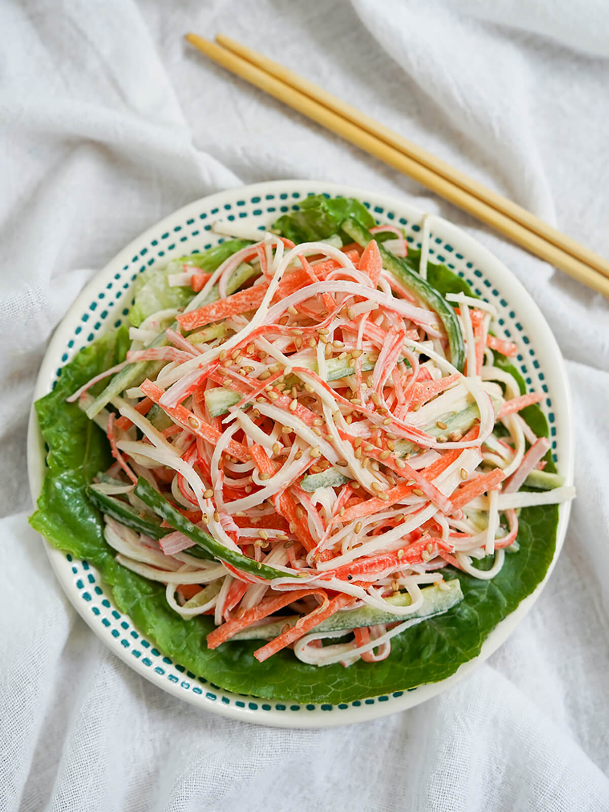 overhead view of small plate of kani salad with chopsticks above plate.