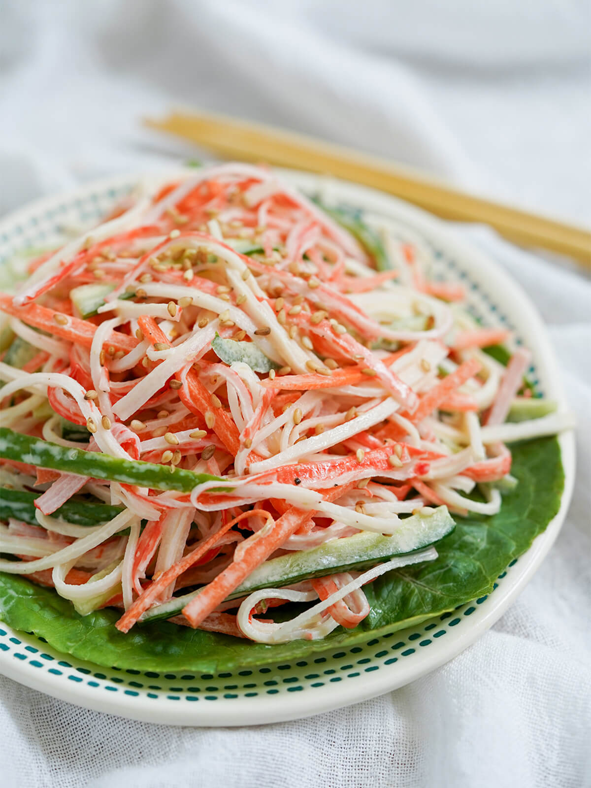 side view of small plate of kani salad with chopsticks blurred in background.