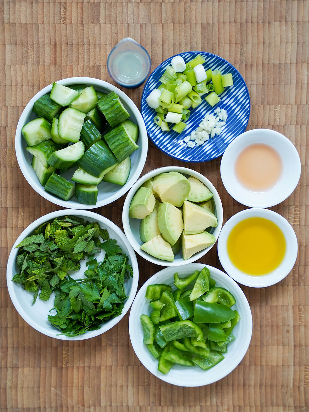 chopped cucumber in dish, and other dishes with chopped avocado, herbs, green pepper, green onions and garlic.