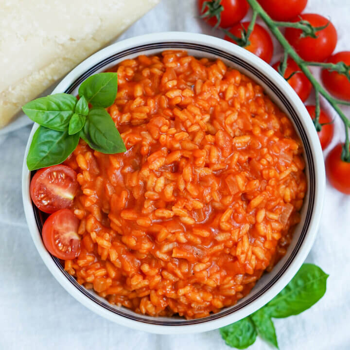 overhead view of bowl of tomato risotto garnished with sprig of basil.