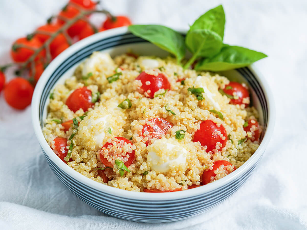 Caprese quinoa salad with beets and avocado - a delicious, light & healthy salad that's perfect for a picnic, potluck or as a side to many a meal! side view of bowl of caprese quinoa salad with stem of tomatoes in background.