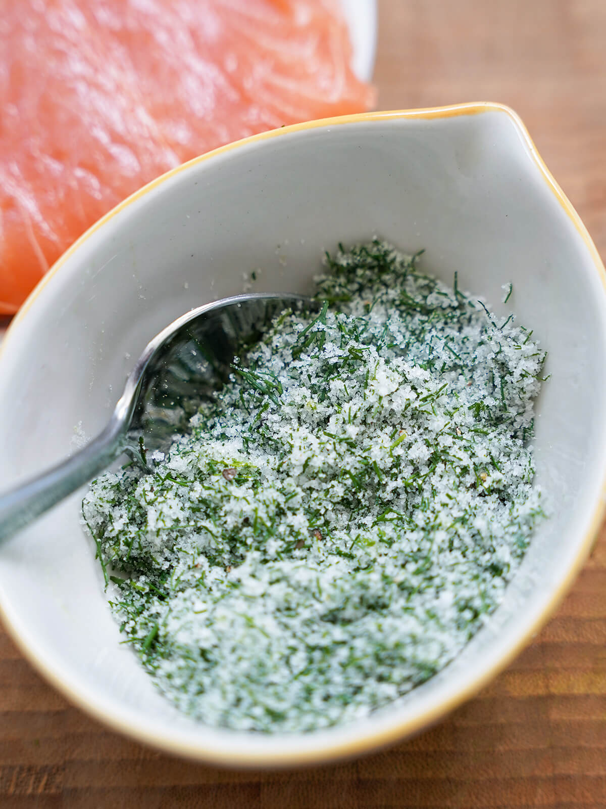 bowl of salt, sugar and dill mixture to cure salmon, in partial view behind.