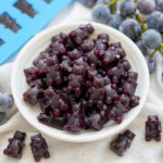 dish filled with grape gummy bears with grapes in background behind.