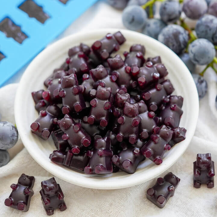 dish filled with grape gummy bears with grapes in background behind.