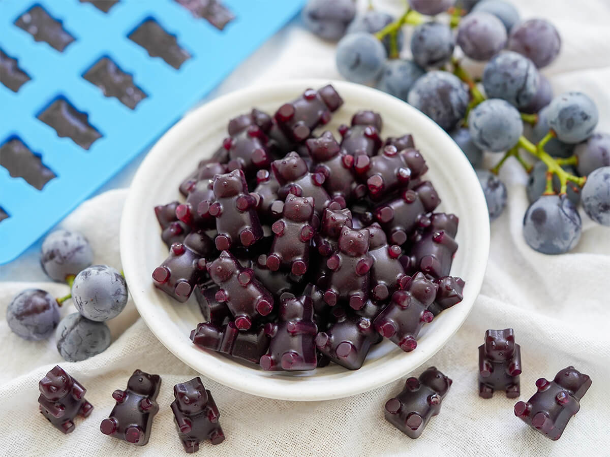 dish of grape gummy bears with a few in front, grapes either side and some still in mould in corner.