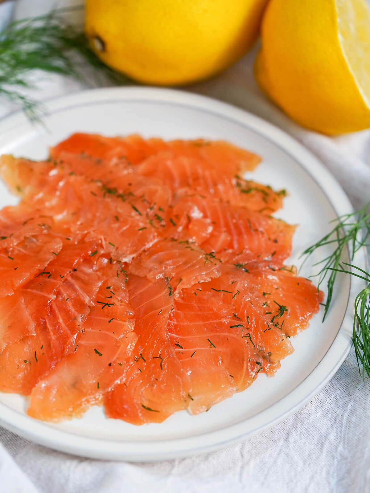 side view of salmon gravlax on plate with lemon behind.