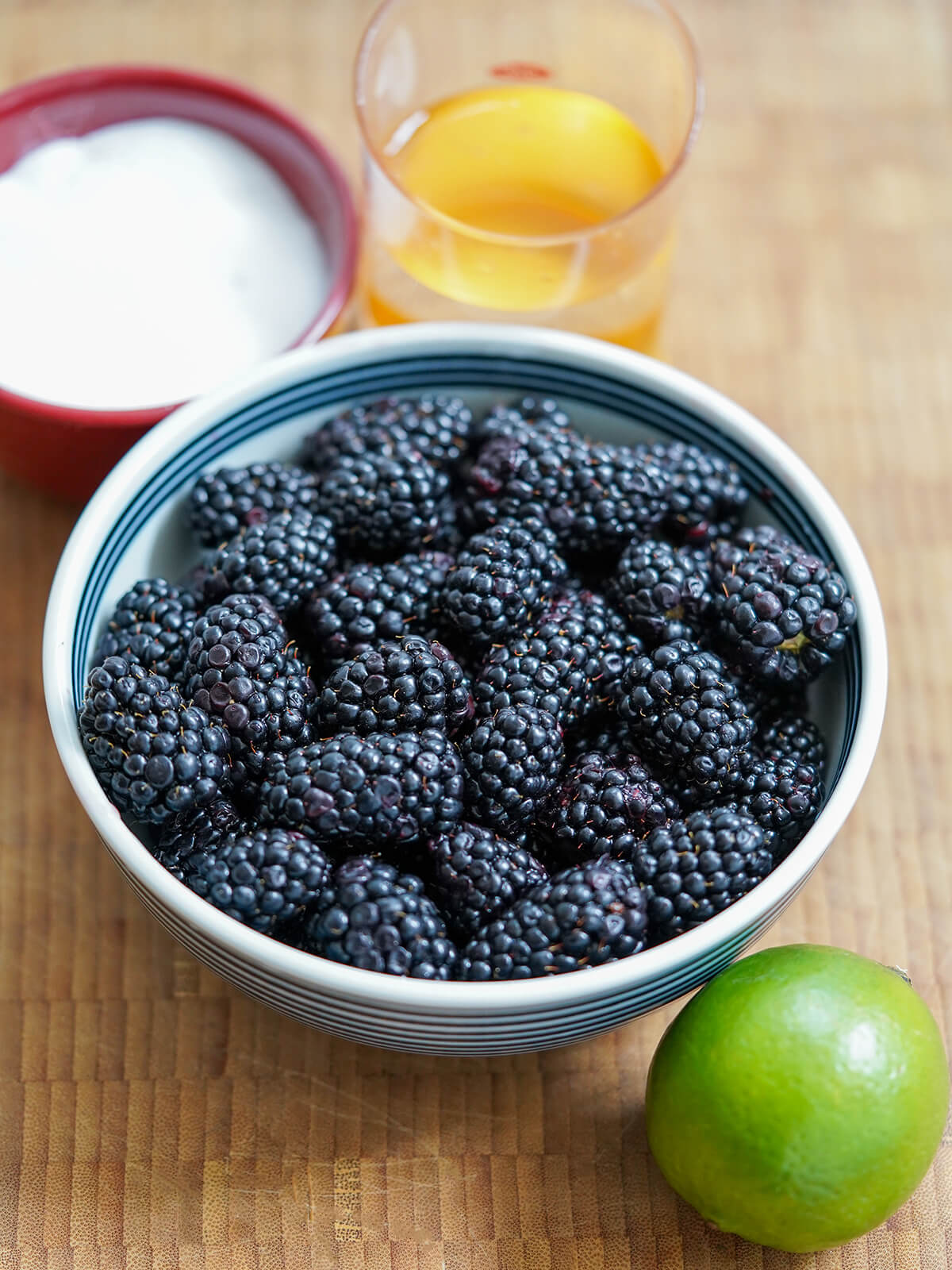 bowl of blackberries with lime in front and dish of sugar and measure of water behind.