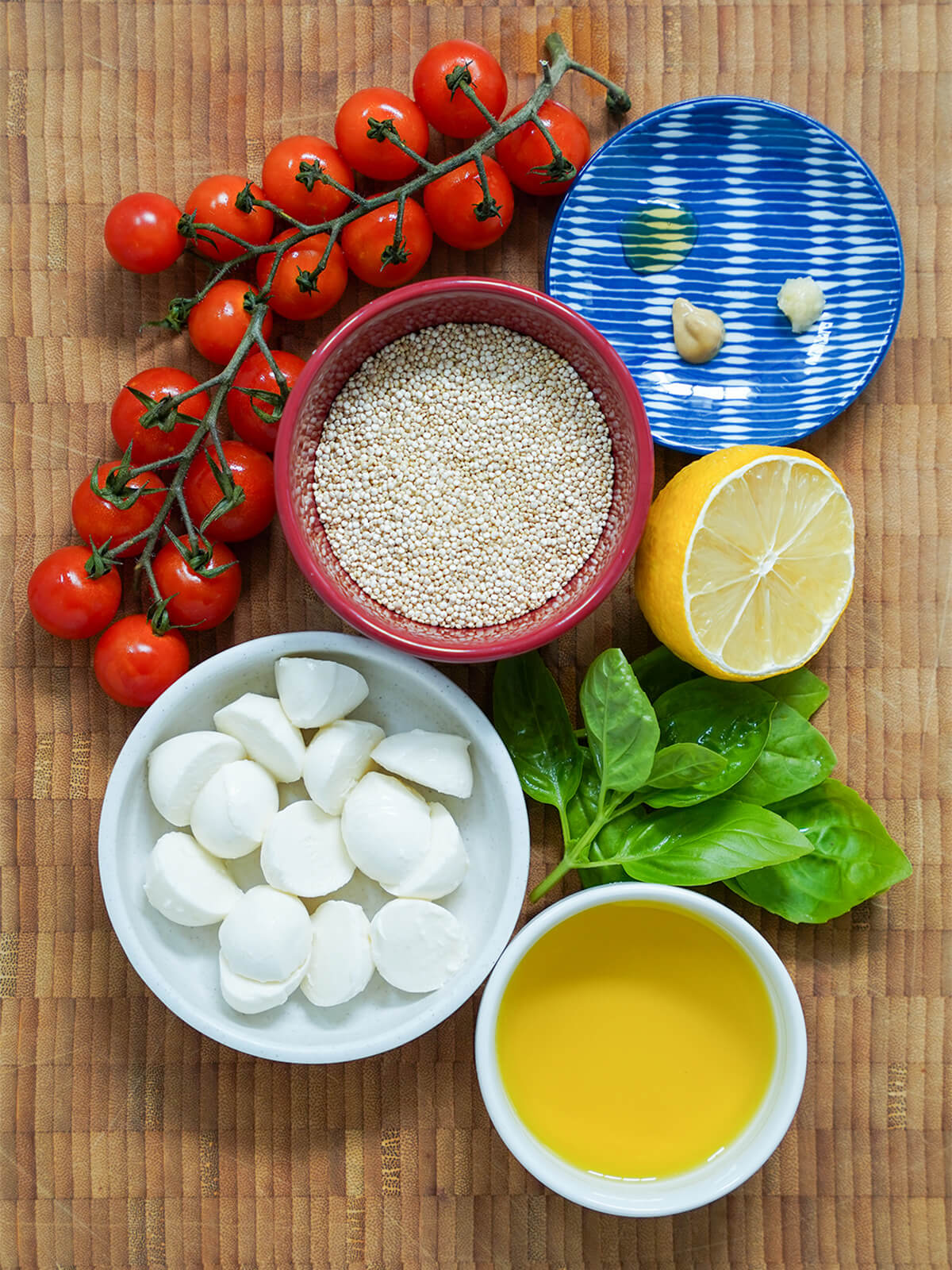 Caprese quinoa salad with beets and avocado ingredients bowls with quinoa, mozzarella, olive oil with part lemon, bunch of basil and cherry tomatoes on vine around.