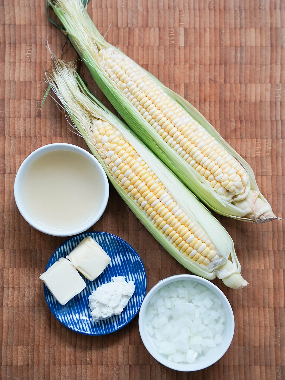 two ears of corn, small dish of stock, bowl of diced onion and dish with butter and goat cheese.