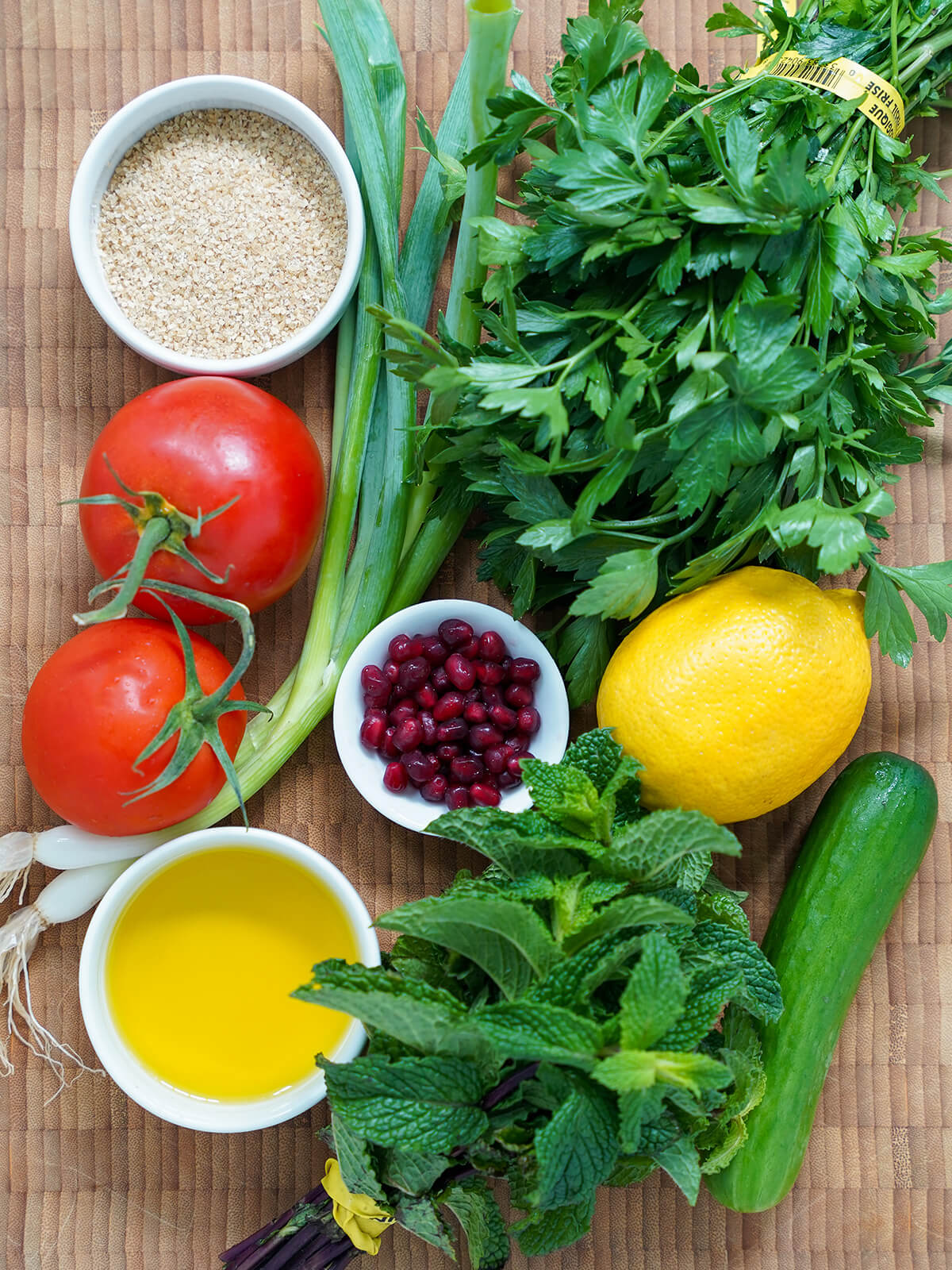 ingredients for tabbouleh with pomegranate bunches of parsley, mint with tomatoes, bulgar, a lemon, cucumber and dish of olive oil