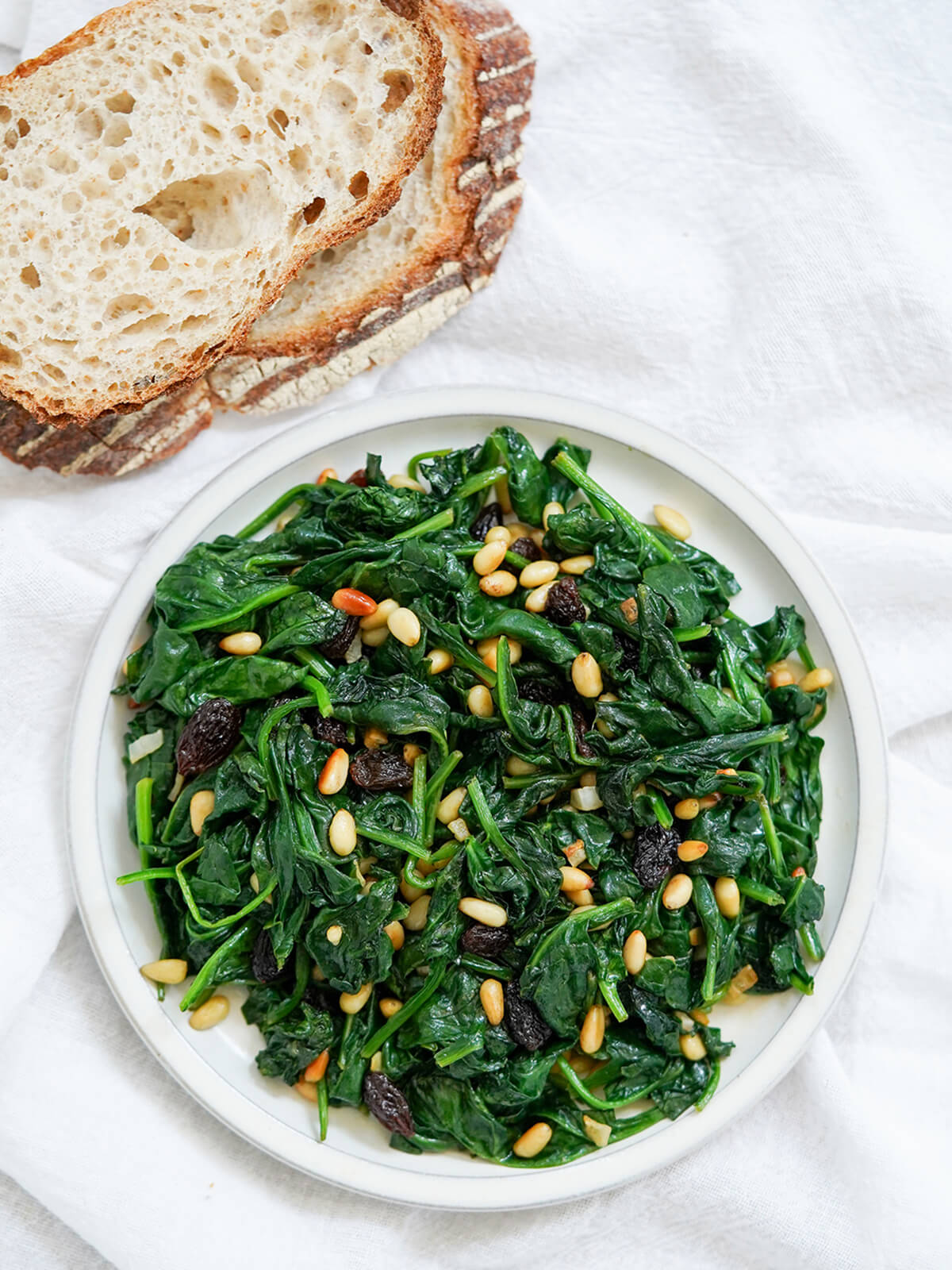 overhead view of plate of Catalan spinach with pine nuts and raisins with bread above plate.