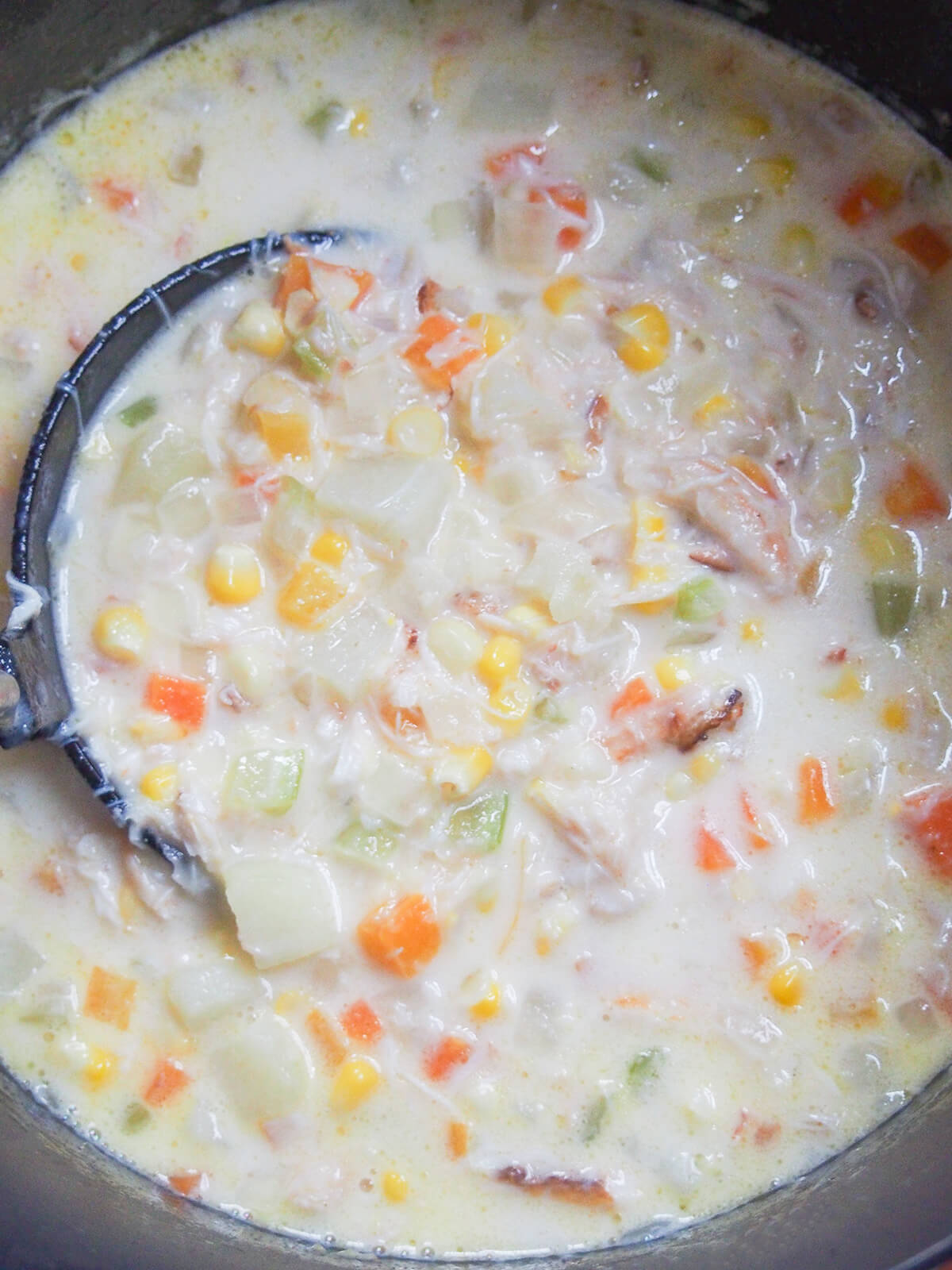 ladle inside pot of crab and corn chowder with lots of chunks of vegetable and crab in it.