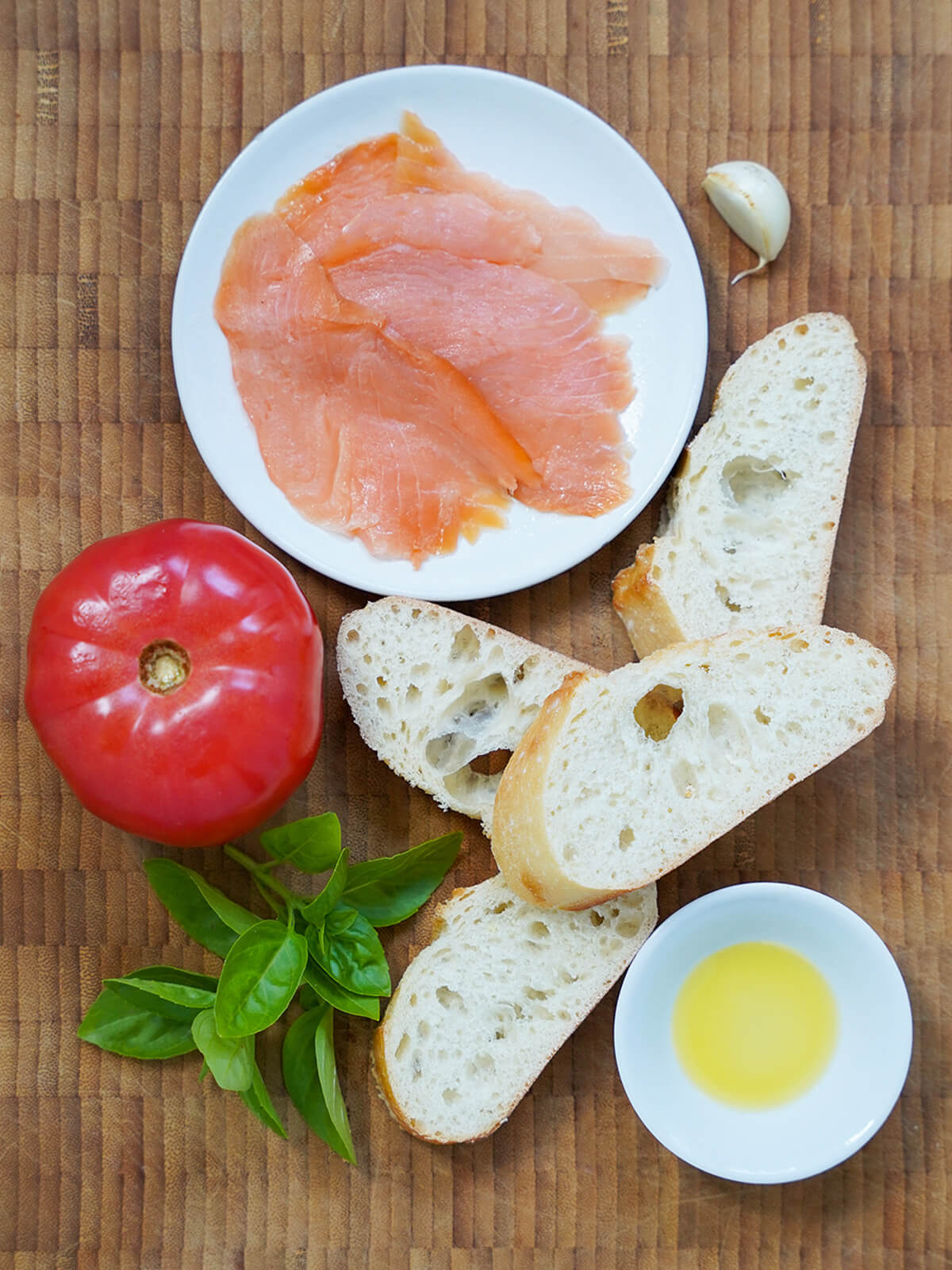 slices of bread, sprigs of basil, tomato and plate with slices of smoked salmon on board.