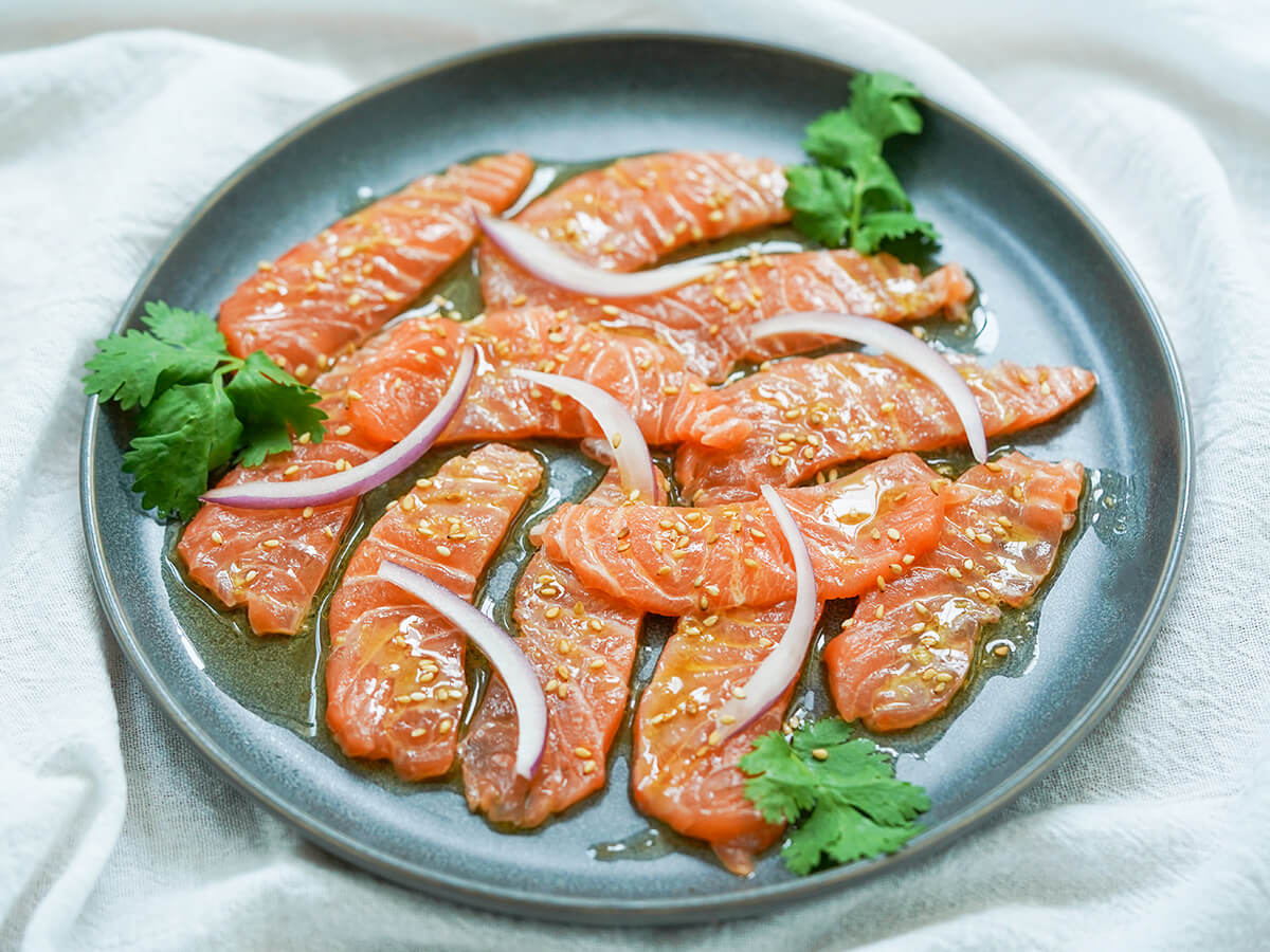 side view of plate of salmon crudo with dressing catching light.