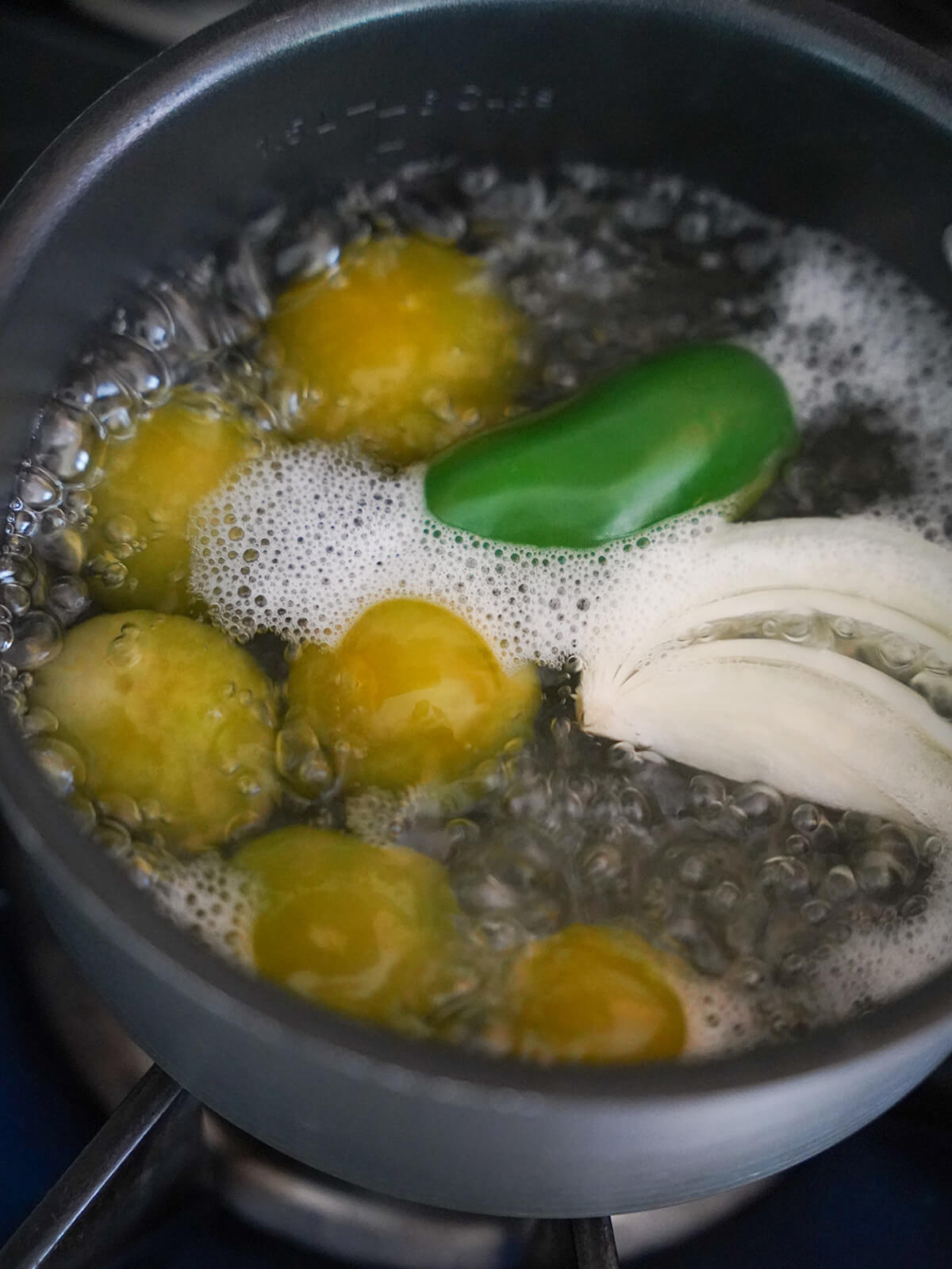 simmering pot with tomatillos, jalepeno and piece of onion in water.
