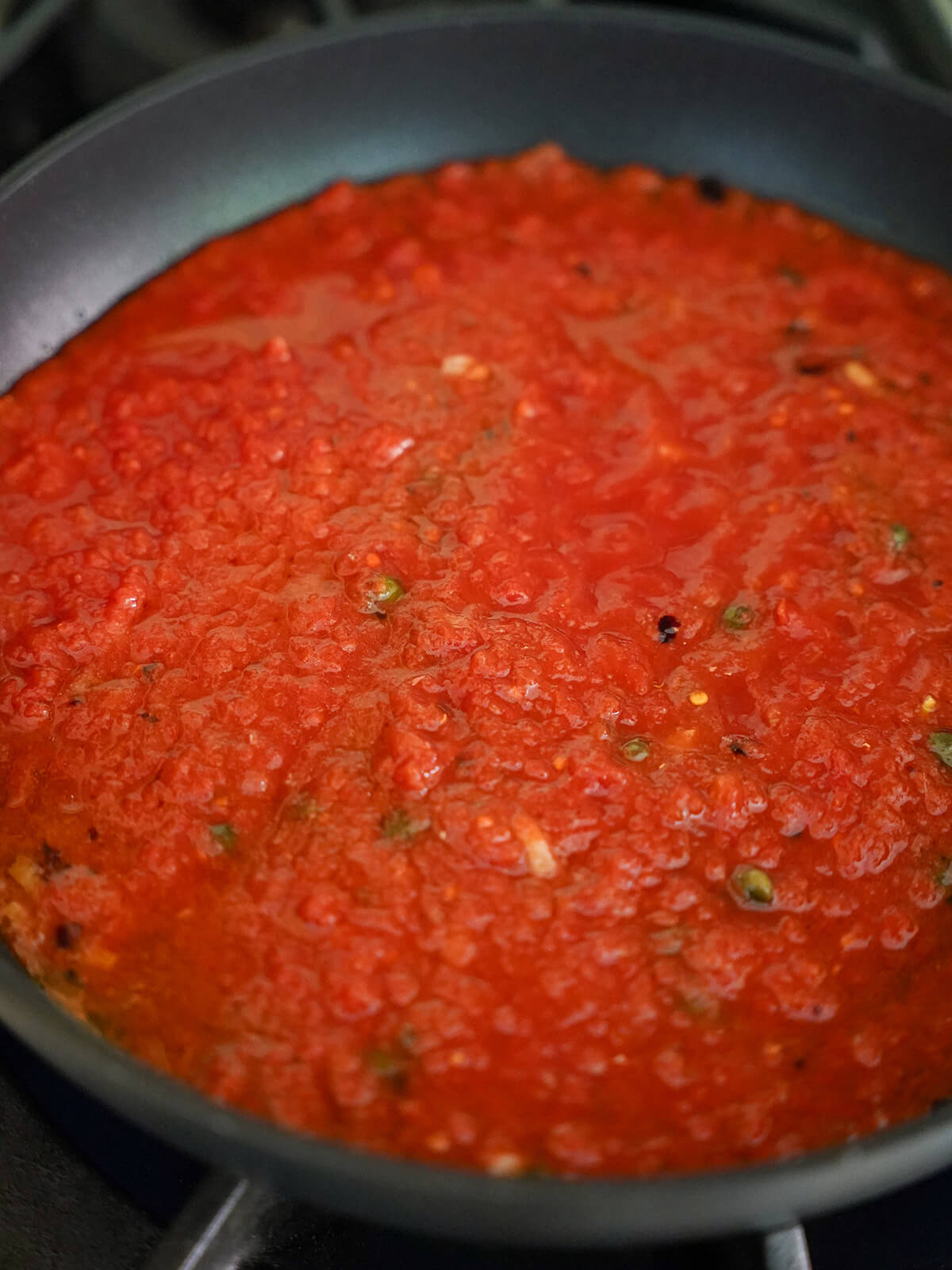 sauce for puttanesca tomato, caper, anchovy and garlic sauce simmering in skillet.