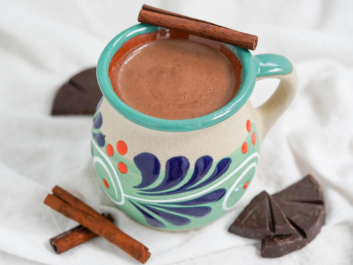 mug of champurrado with cinnamon sticks and pieces of Mexican chocolate to sides.