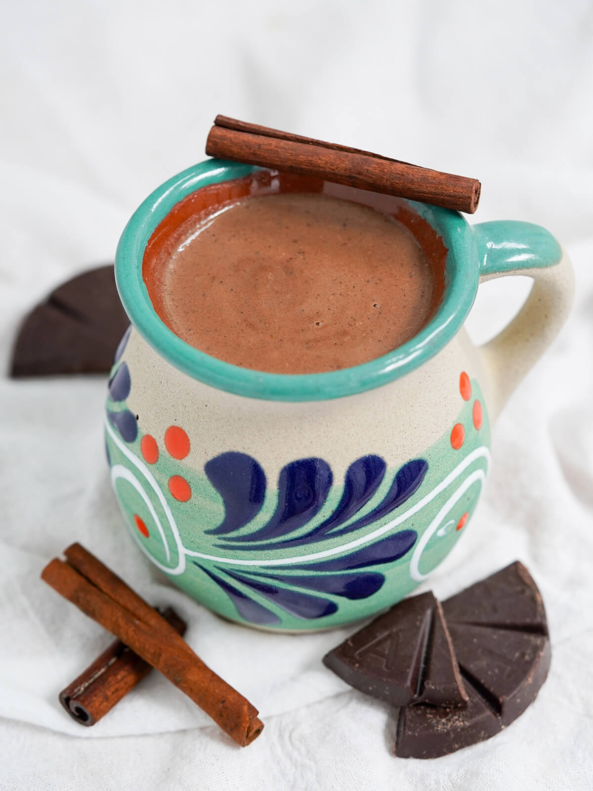 mug of champurrado with cinnamon sticks on top and in front and pieces of Mexican chocolate.