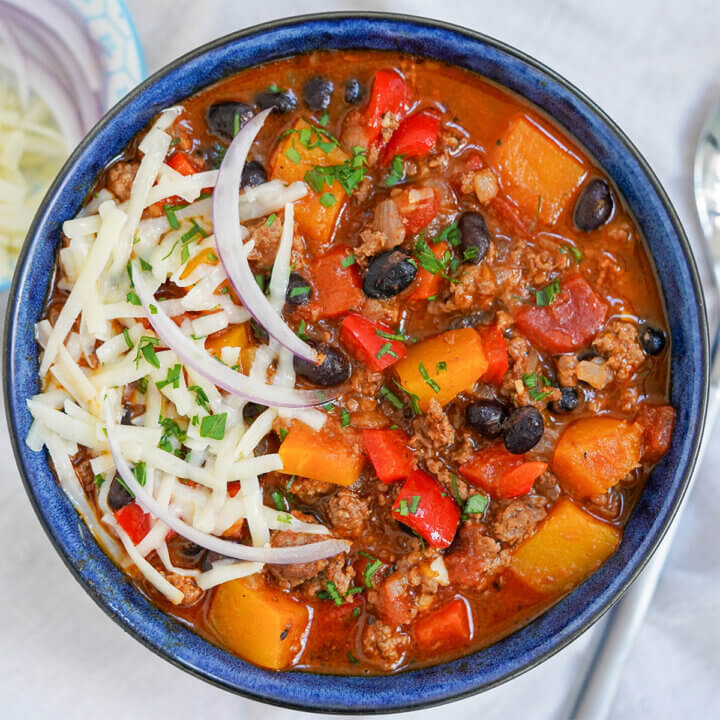 overhead view of bowl of chili with butternut squash garnished with grated cheese.