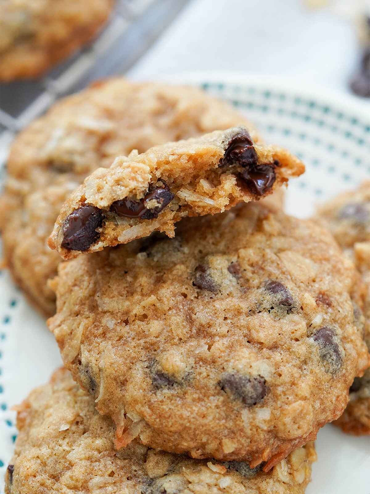 close up of a cookie resting on others showing oats, coconut and melty chocolate chips inside.