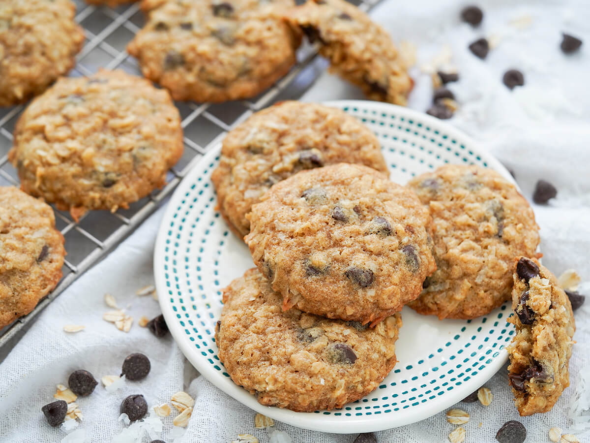 plate of coconut oatmeal chocolate chip cookies with a half cookie resting on side and more cookies on rack to other side.
