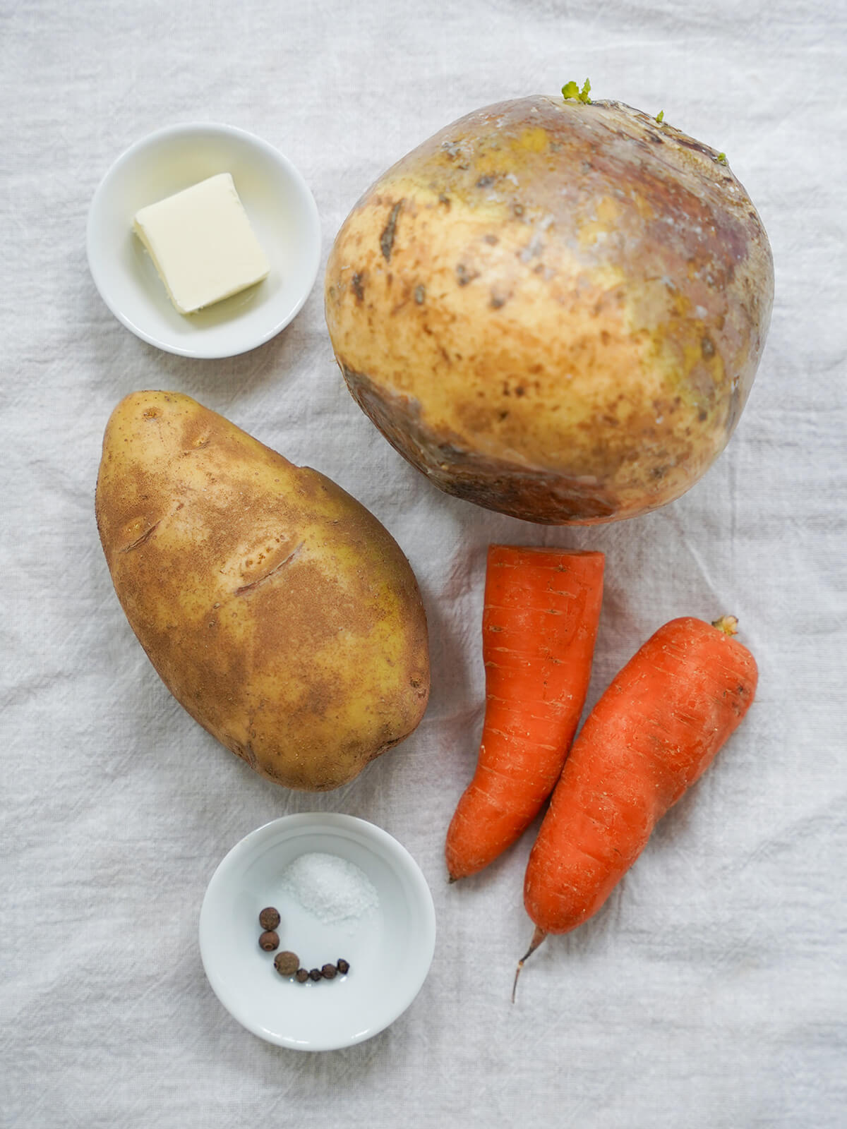rutabaga, potato, carrots on cloth with dishes with butter, salt and peppercorns.